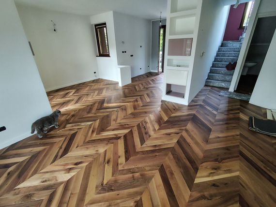 Stanza bianca vuota con pavimento in legno a spina di pesce e luce intensa proveniente dalla finestra.