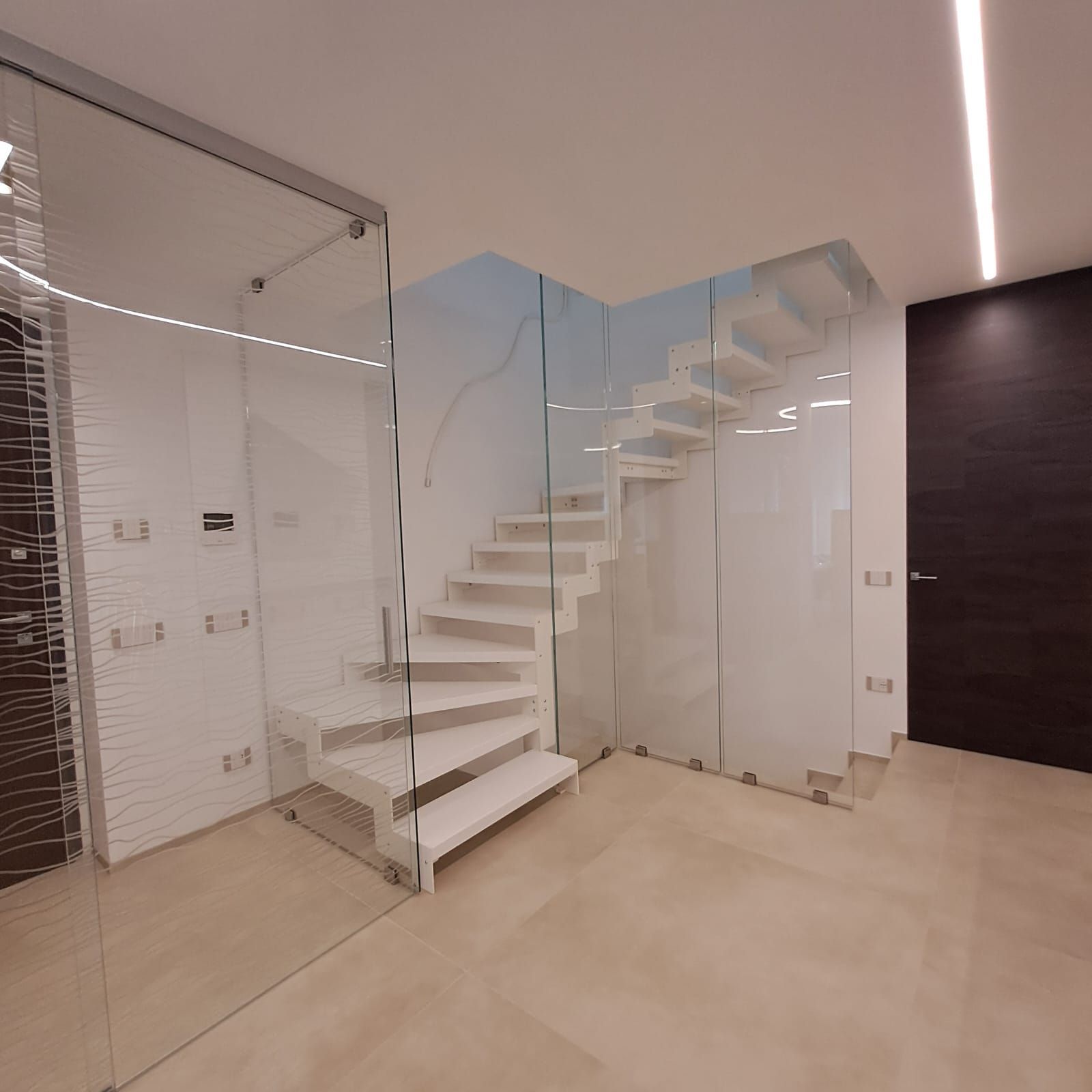 Interno moderno con scala bianca, pareti in vetro e porta in legno scuro in una stanza minimalista