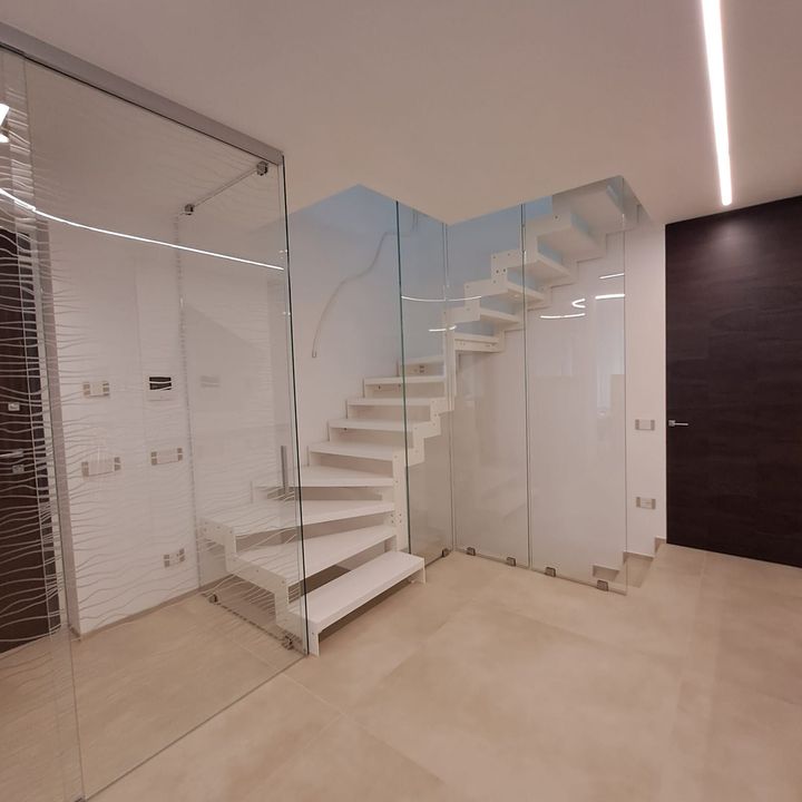 Interni moderni con scala bianca, ringhiera in vetro, parete a specchio e porta in legno scuro.
