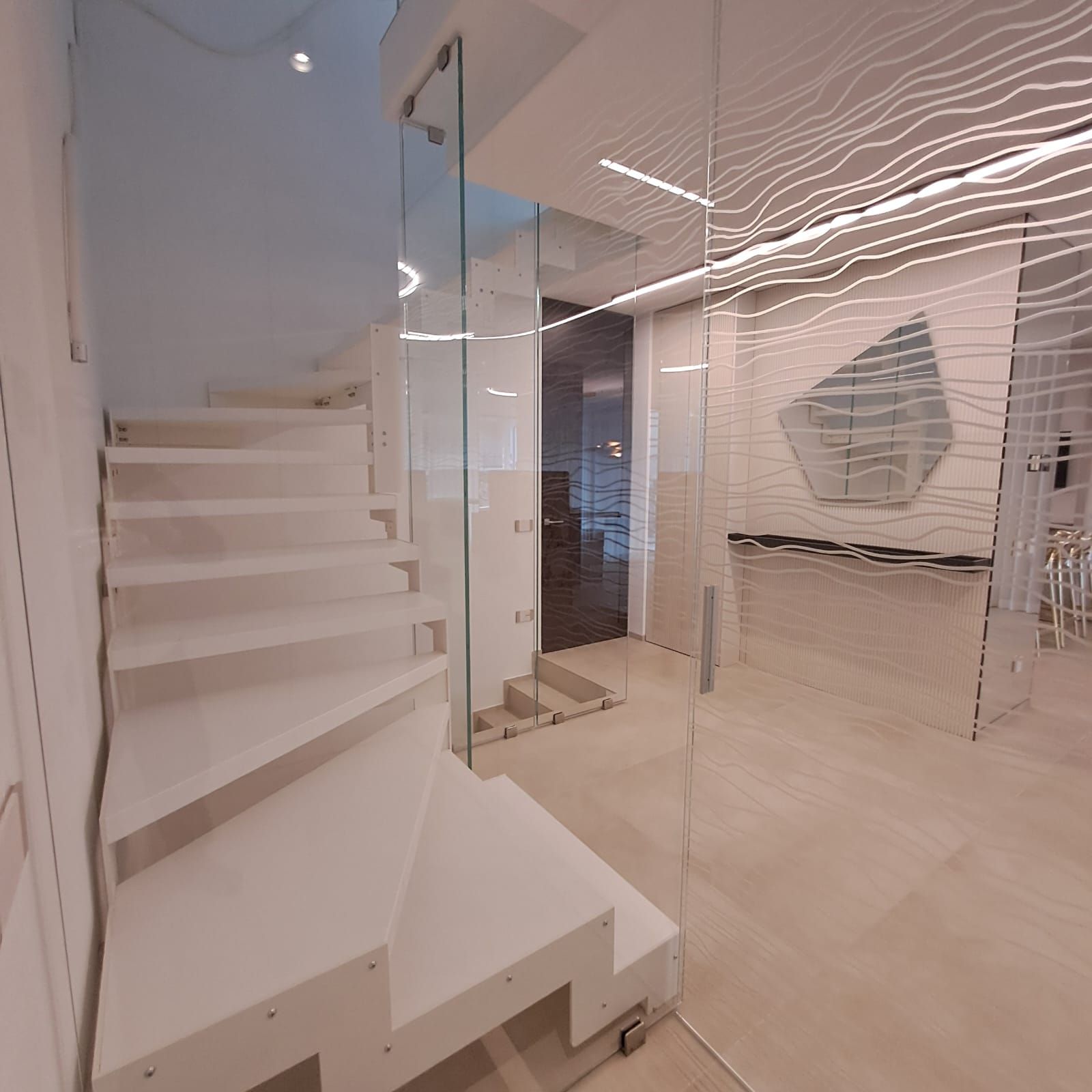 Interni moderni e minimalisti con scala bianca, parete in vetro e lampade a soffitto ondulate.