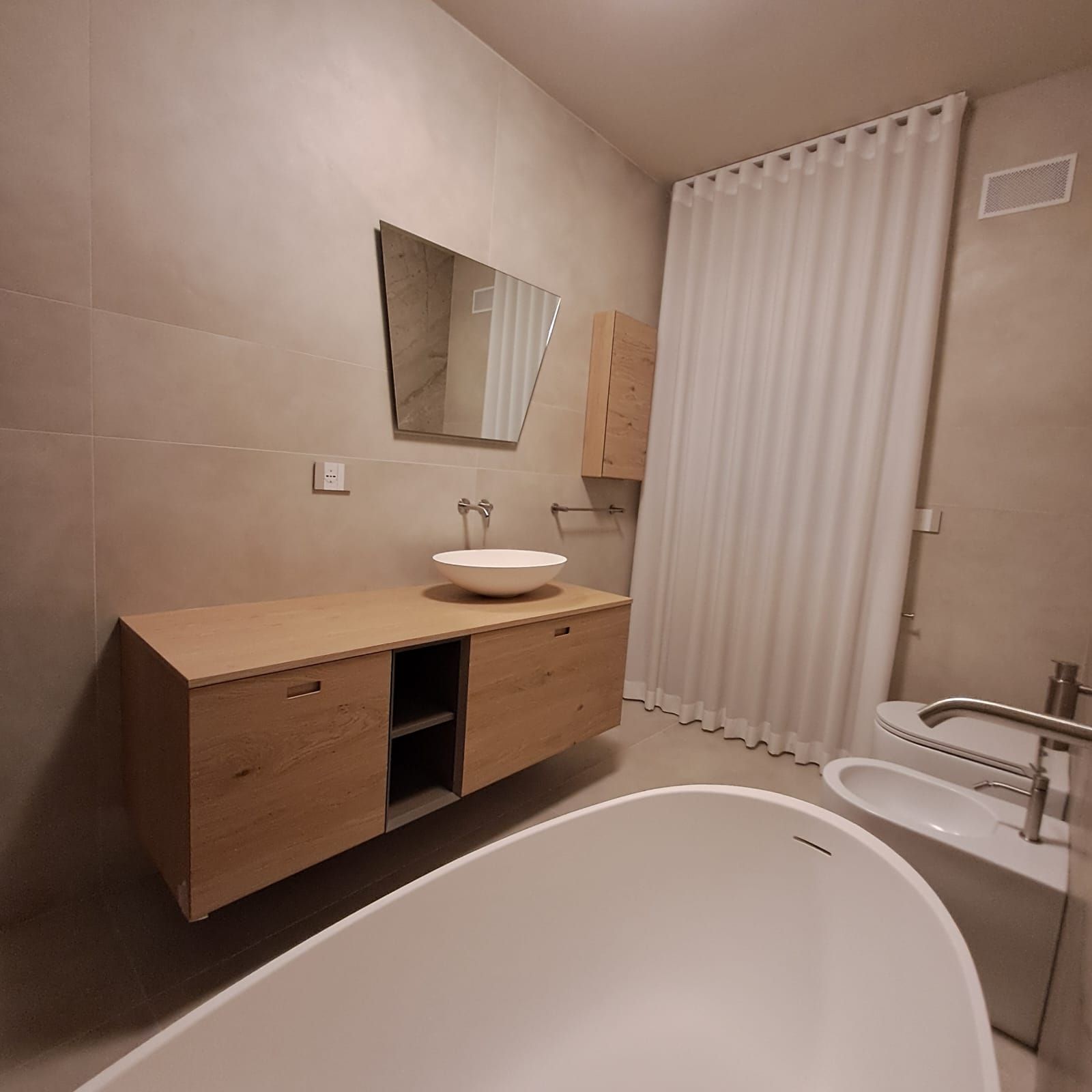 Bagno moderno con vasca da bagno, mobiletto in legno, lavabo rotondo, specchio e pareti beige.