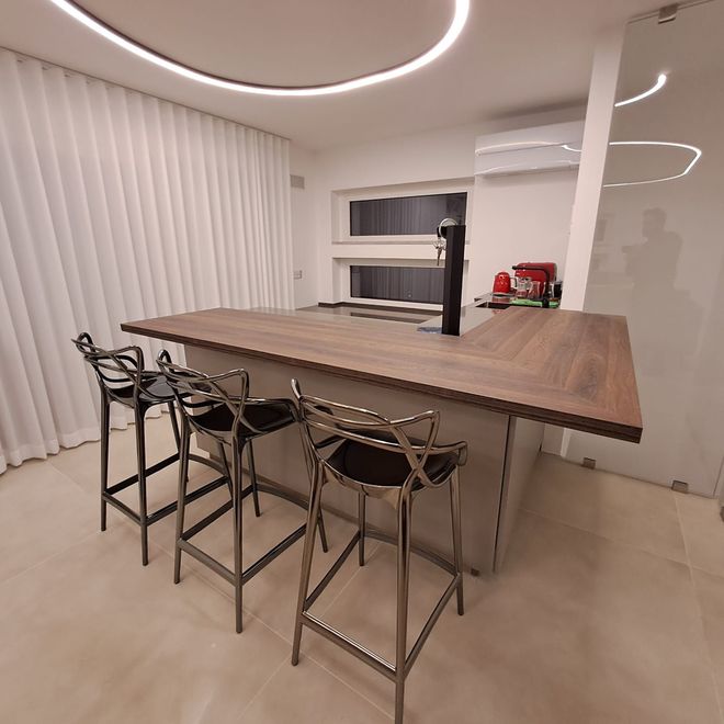 Cucina moderna con grande isola in legno, quattro sgabelli da bar e pareti bianche con faretti ad anello sul soffitto.