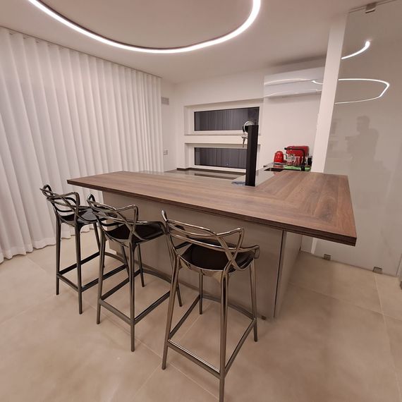 Cucina moderna con grande isola in legno, quattro sgabelli da bar e illuminazione minimalista.