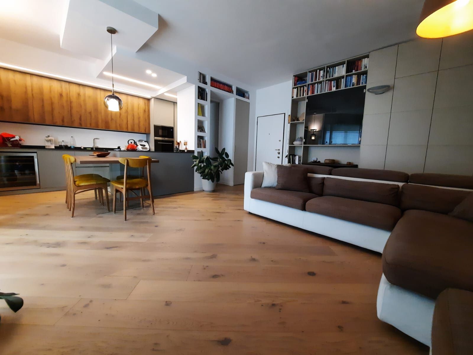 Soggiorno moderno a pianta aperta con cucina, pavimento in legno e divano componibile in tonalità neutre.