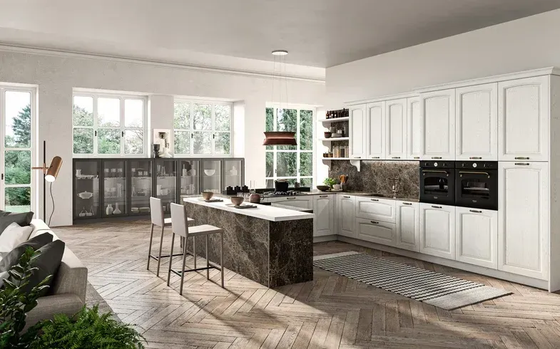 Cucina moderna e luminosa con mobili bianchi, isola centrale, ampie finestre e pavimento in legno.