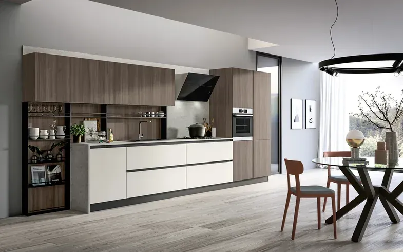 Cucina e zona pranzo moderne a pianta aperta con mobili in legno, isola bianca e lampadario nero vicino alle grandi finestre.