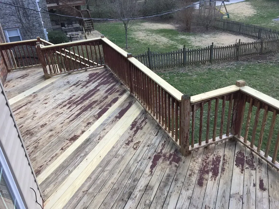 Weathered wooden deck with railing, overlooking a backyard.