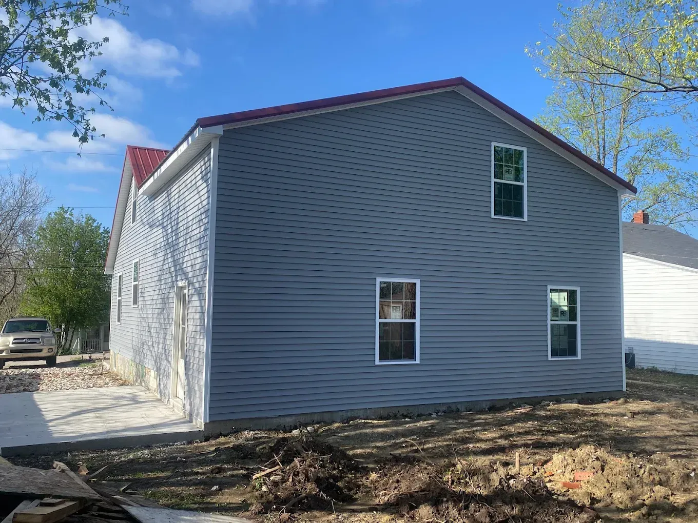 Two-story house with blue siding and a red roof, a concrete walkway, and a bright sky.