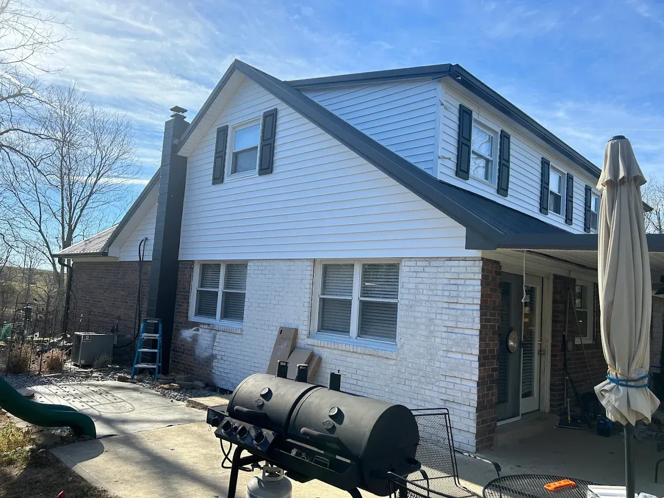 Two-story house with white siding and black roof. A brick chimney and barbecue grill are in the yard.