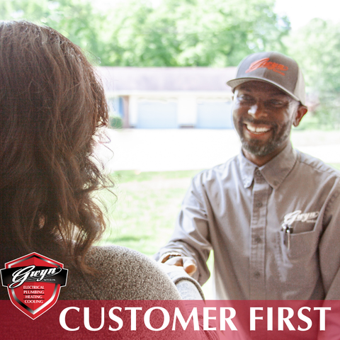 Smiling worker in gray uniform and cap greeting a person; red banner reads “CUSTOMER FIRST.”
