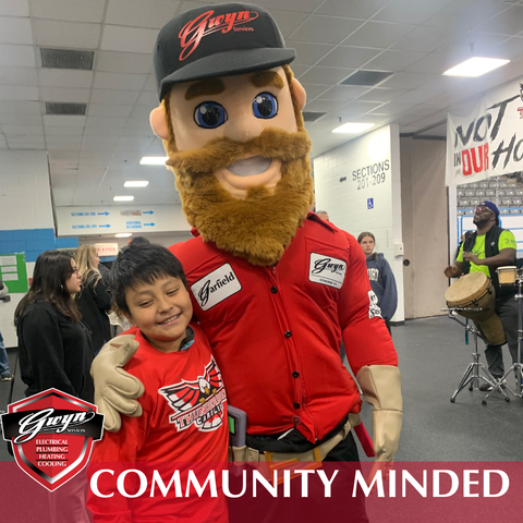 Mascot in red shirt hugs smiling child at indoor community event, with “Community Mined” banner.