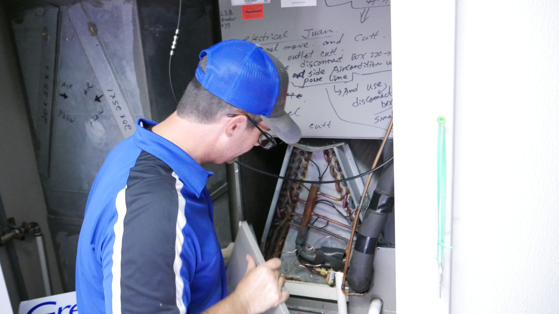 Worker in blue cap inspecting electrical wiring inside a utility panel