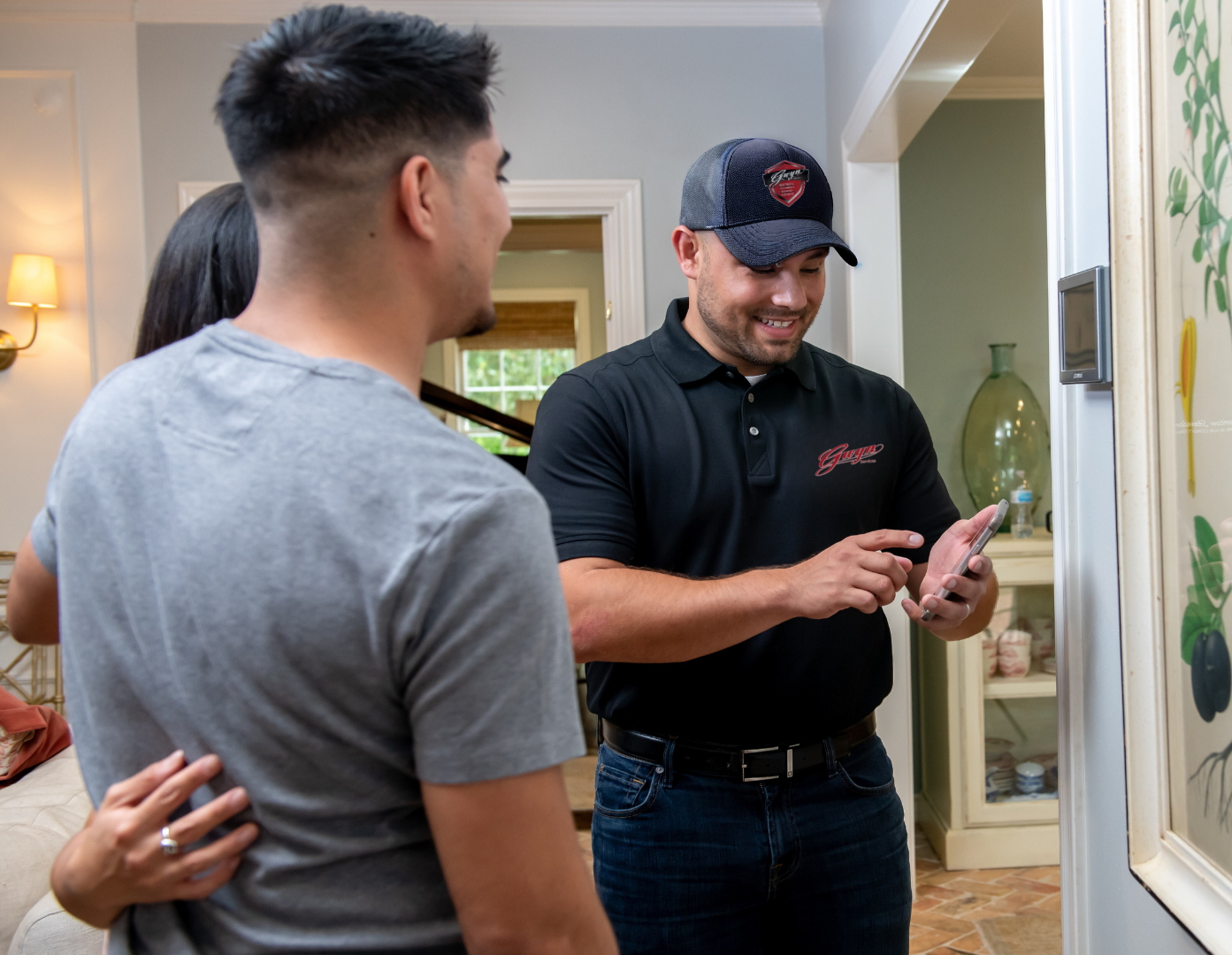 Two men standing in a hallway, one pointing at a phone while the other looks on.