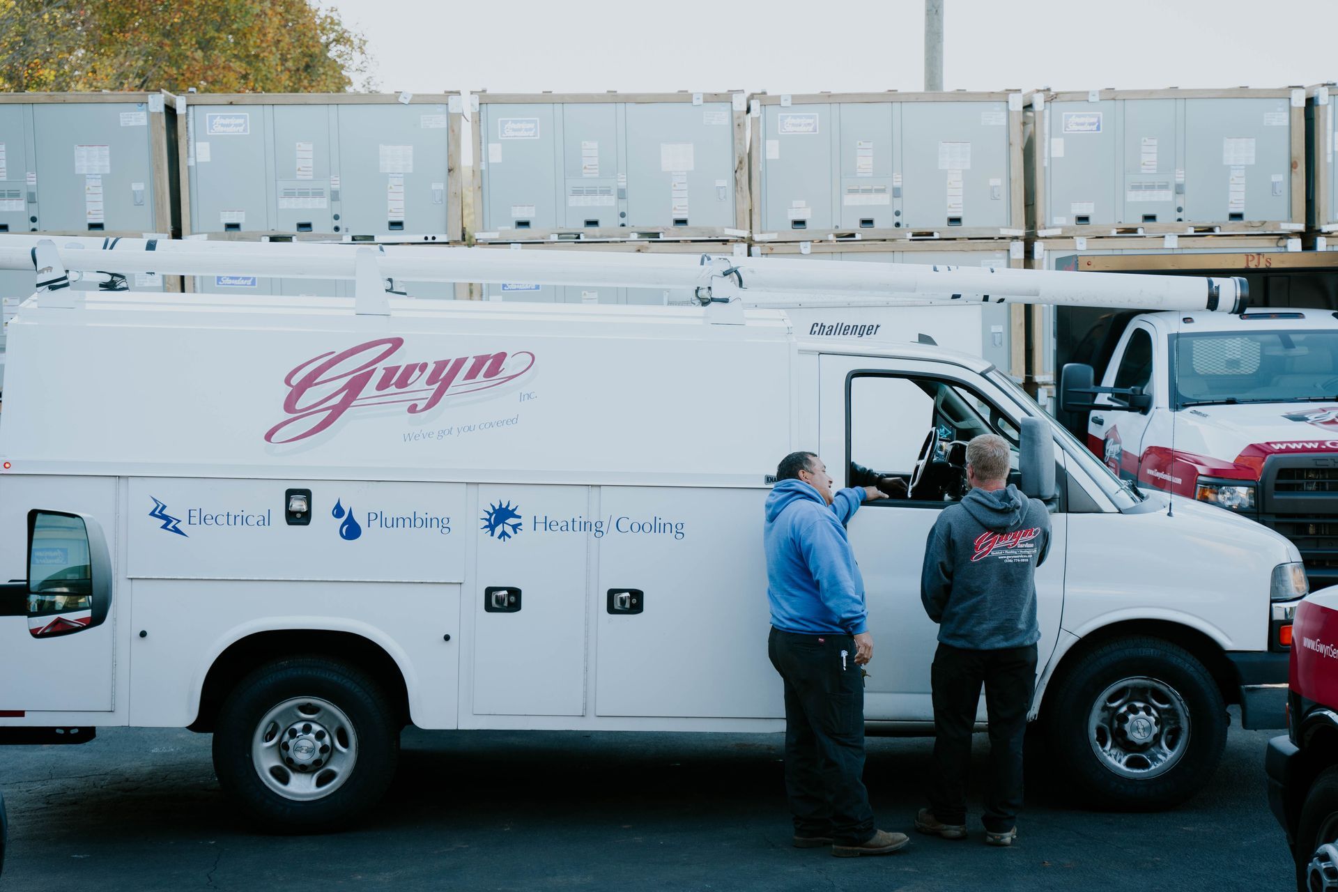 White service truck with two workers beside it in a parking lot, with stacked containers in the background