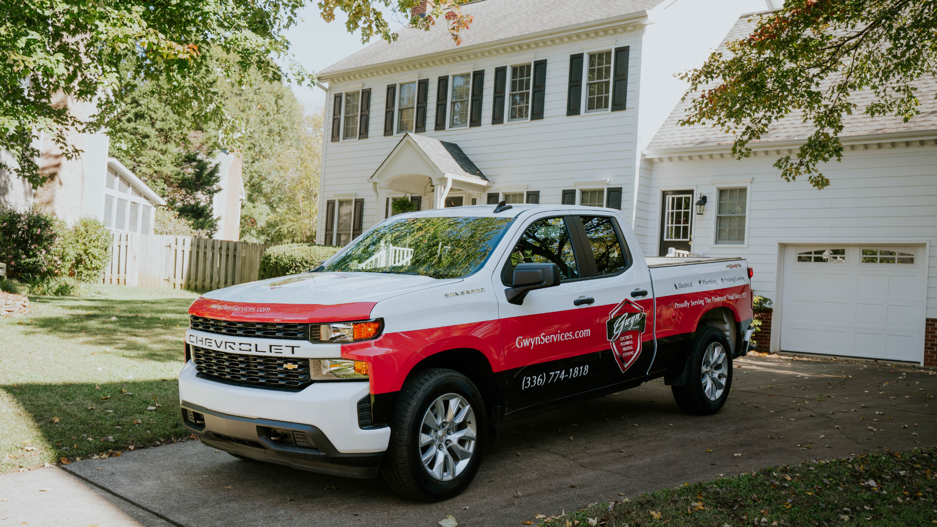 Red-and-white utility pickup truck parked in a suburban driveway in front of a house.