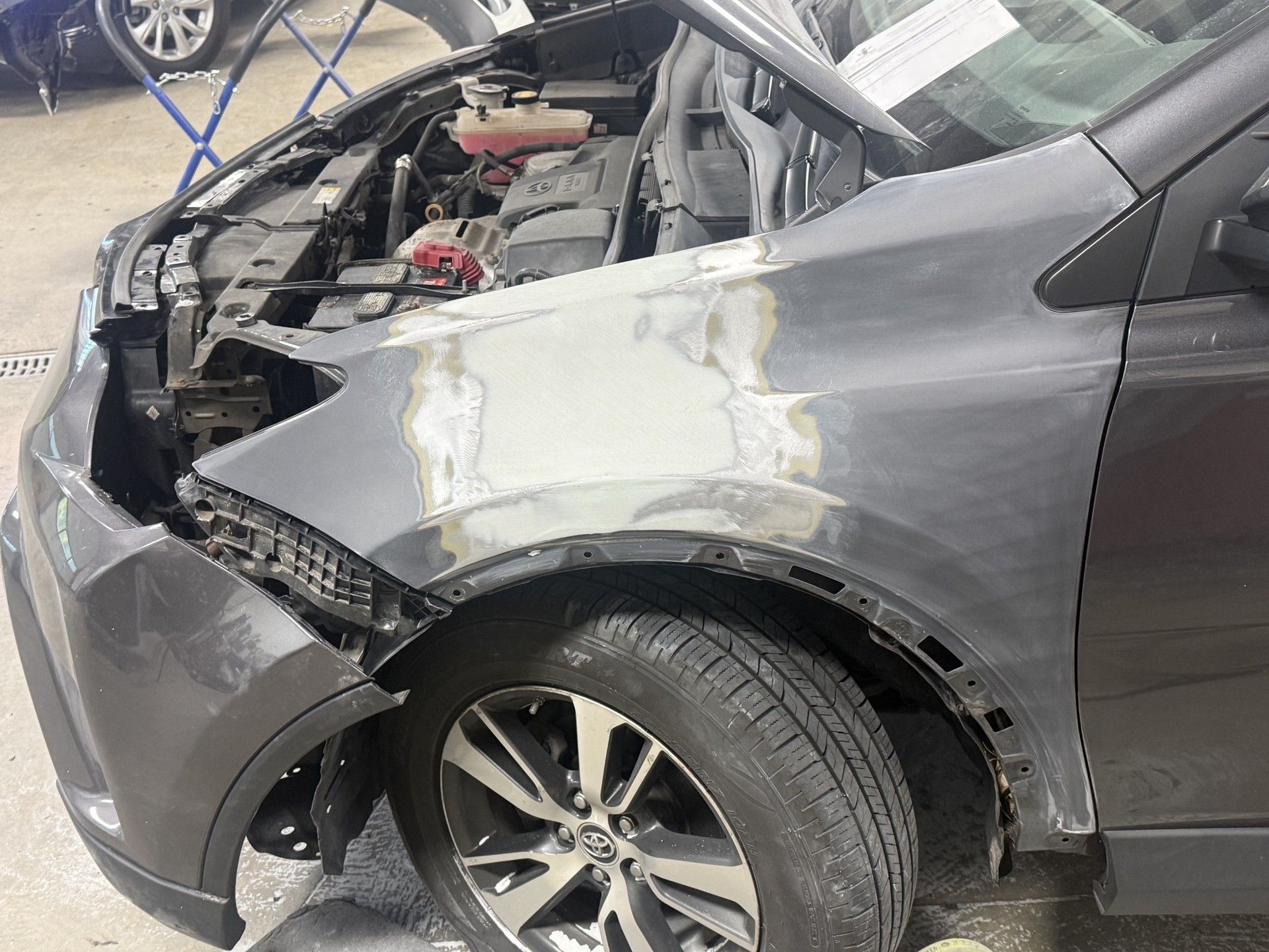 Damaged gray car with front-end and fender collision damage in a parking lot