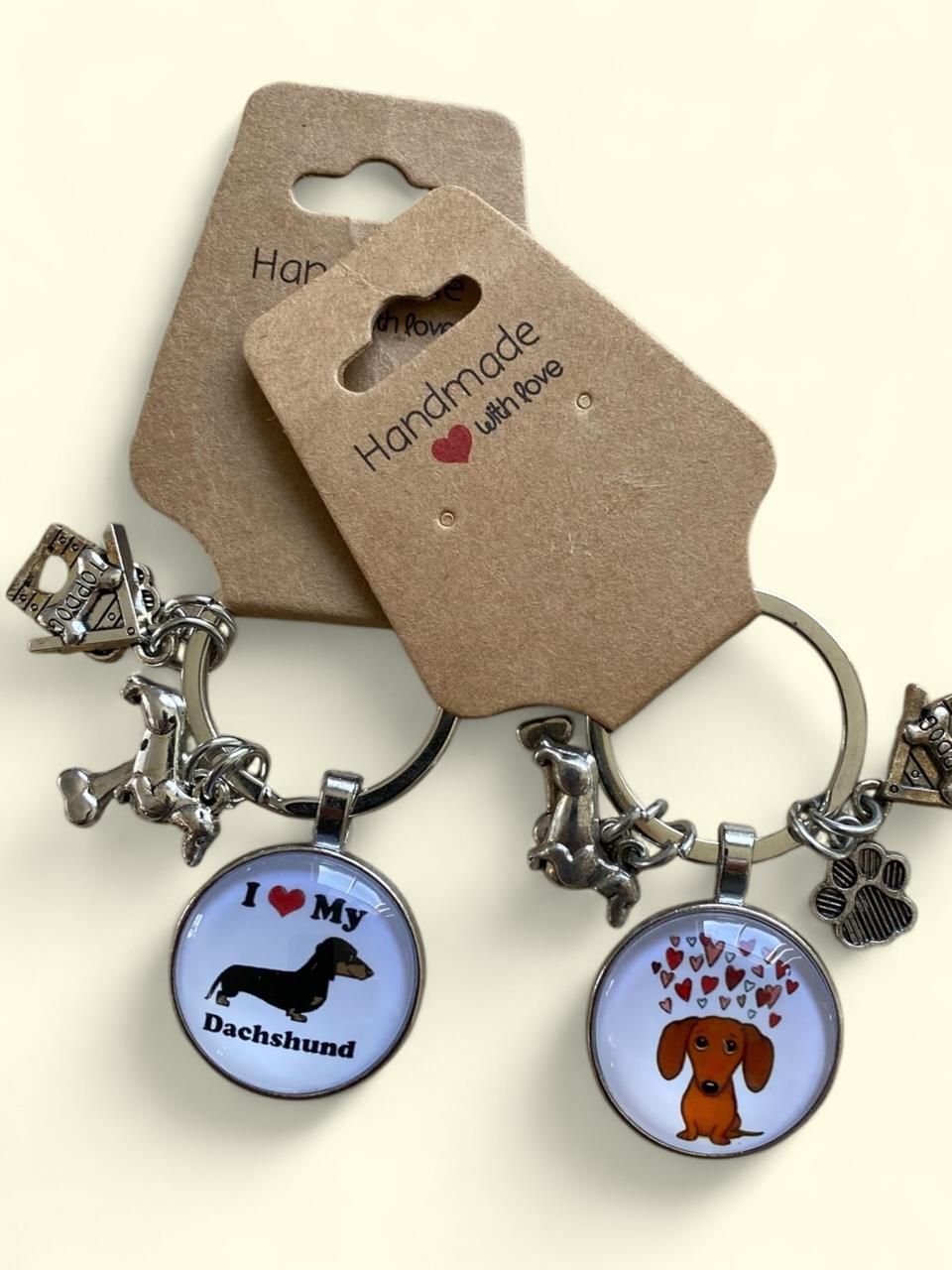 Llaveros con temática canina, con colgantes redondos de esmalte y etiquetas en forma de hueso sobre un fondo beige.