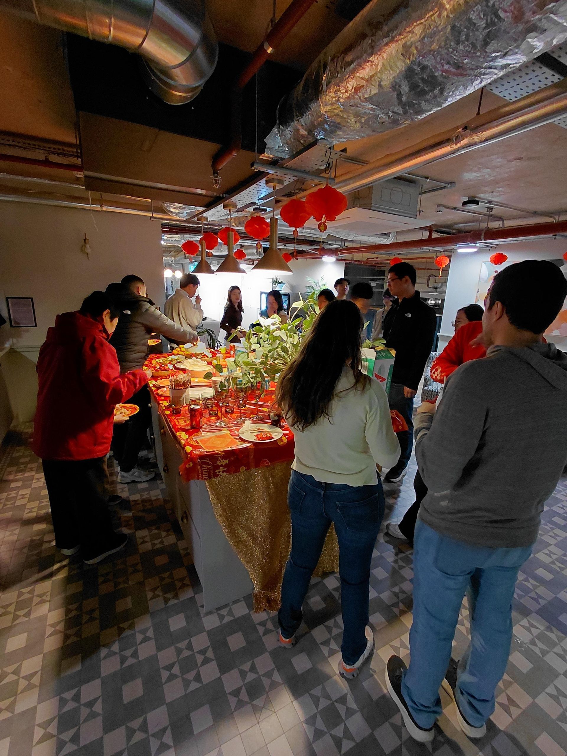 People gathered around a buffet table in a room with exposed ducts and red hanging decorations.
