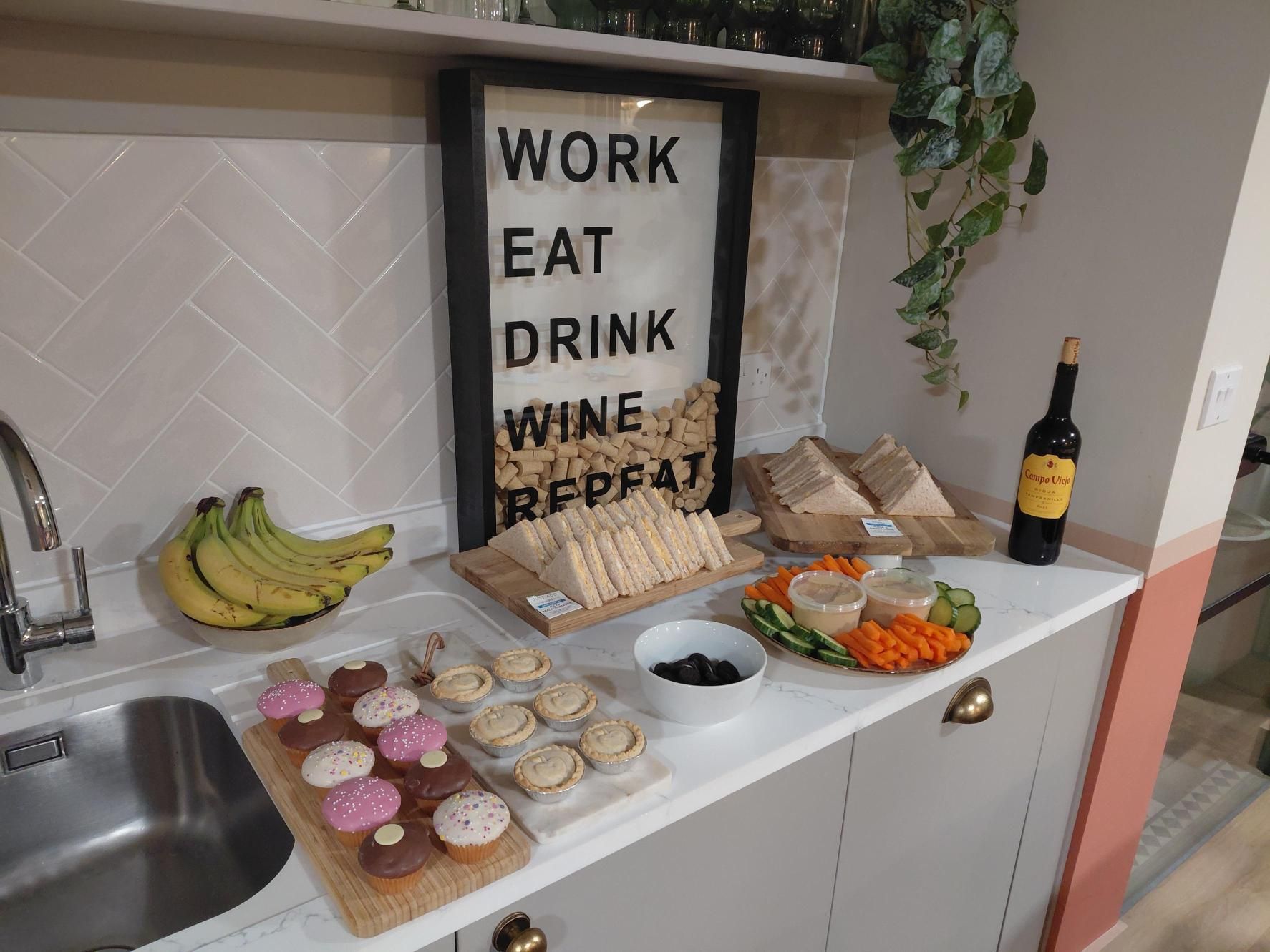 Counter with snacks, fruit, wine bottle, and a sign reading “WORK EAT DRINK WINE REPEAT”