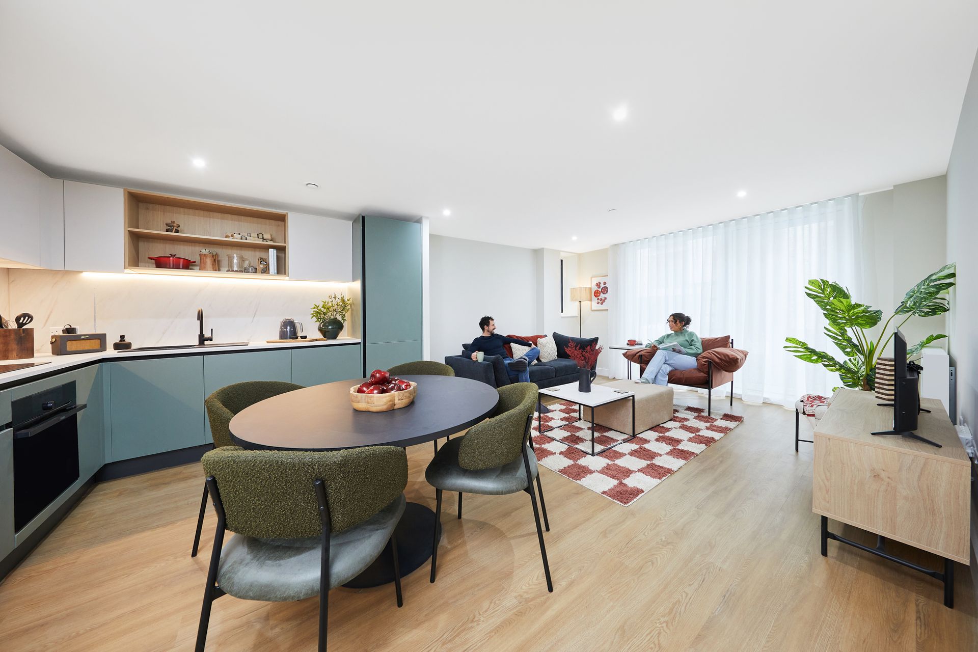 Modern open-plan kitchen and living room with round dining table, red rug, sofa, and large windows