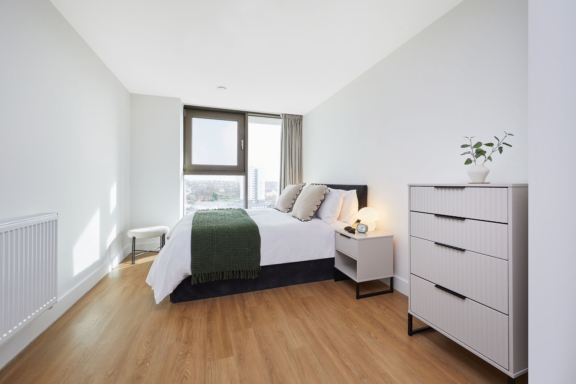 Bright minimalist bedroom with white walls, wood floor, bed, dresser, and window seating area