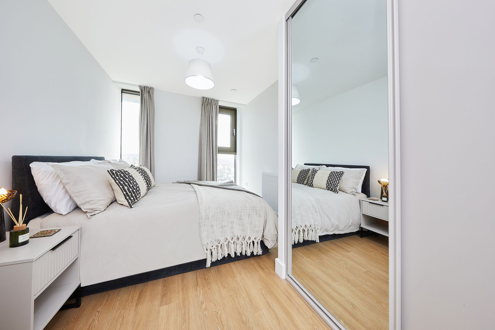 Bright bedroom with bed, mirrored closet, and wood flooring in soft gray and white tones