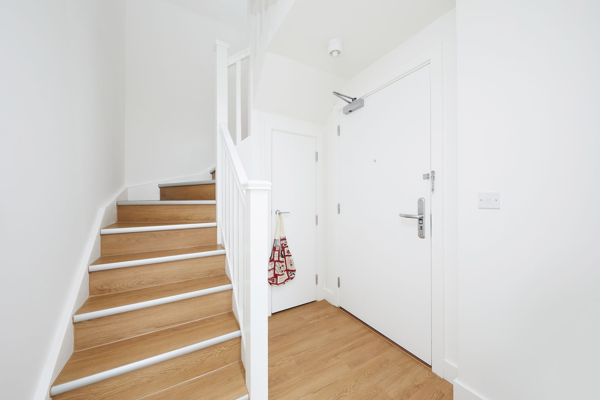Bright white entry hall with wooden stairs and a front door.
