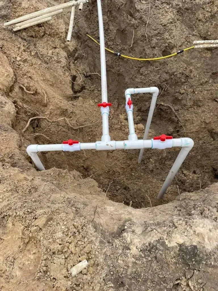 White PVC pipes with red valves installed in a dirt trench at a construction site