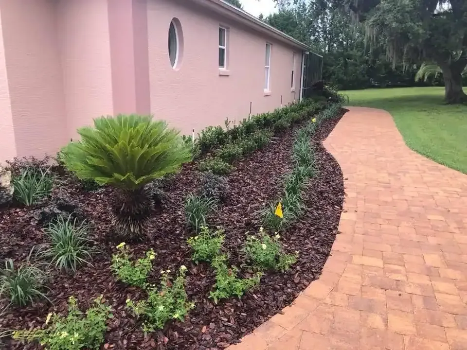Curved brick walkway beside a pink house with dark mulch and green landscaping.