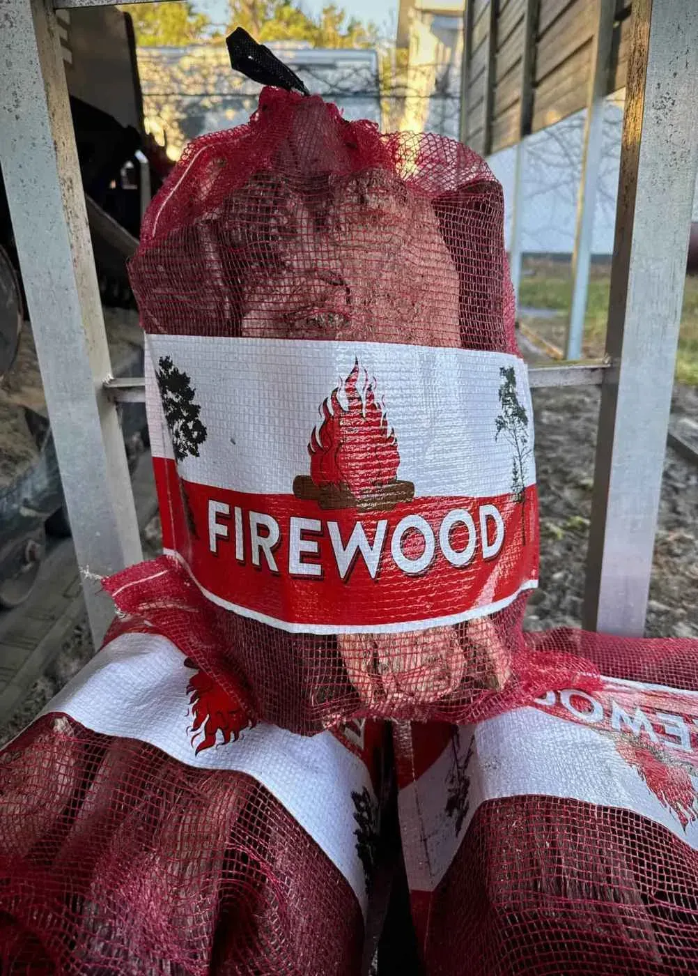 Red mesh bags of firewood stacked outdoors with a white and red FIREWOOD label