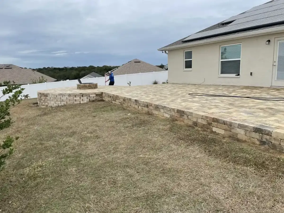 Coastal backyard with stone patio, grassy yard, and a person in blue near white houses under cloudy sky