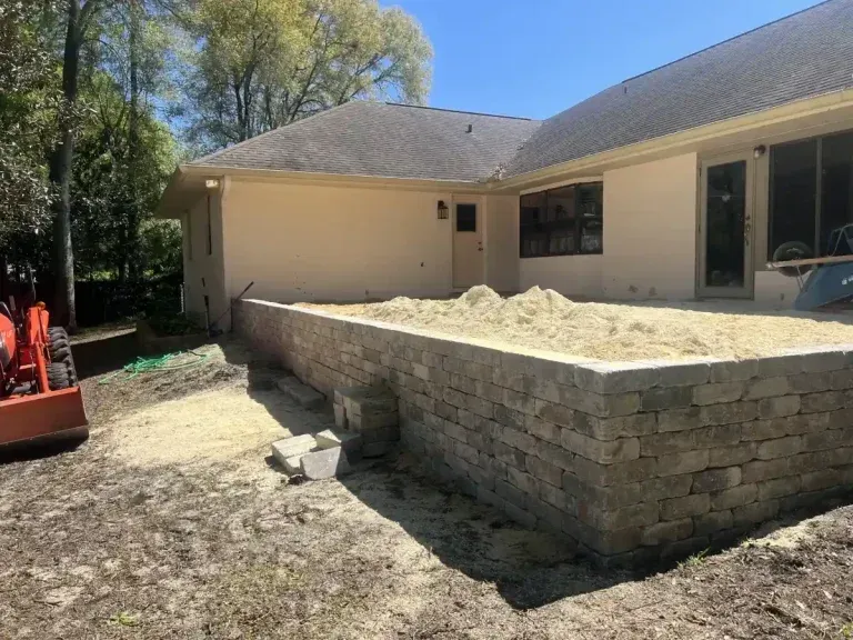 Backyard patio with stacked stone retaining wall and a sandbox beside a beige house