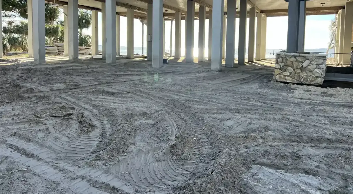 Empty concrete interior with columns, tire tracks on the floor, and a stone wall section near the right side.