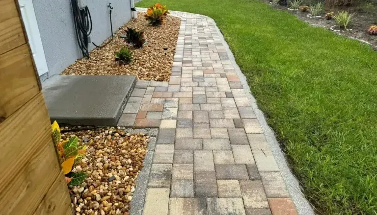Brick paver walkway beside house, bordered by gravel and lawn, leading past a front entry step