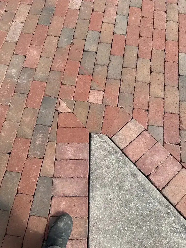 Brick walkway with a concrete corner and a shoe at the bottom left.