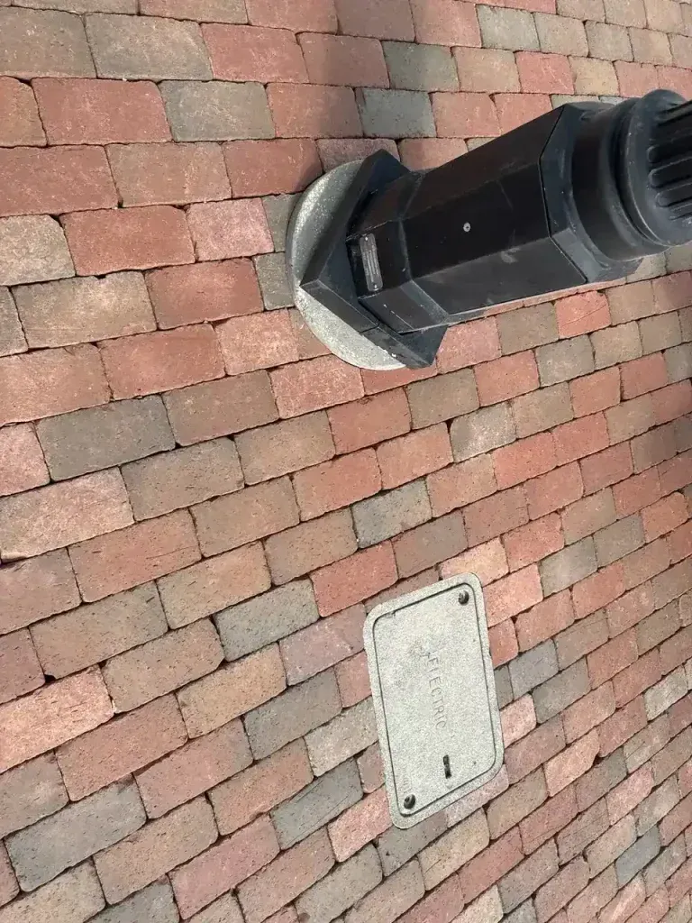 Red brick rooftop with a black vent pipe and a small white access panel.
