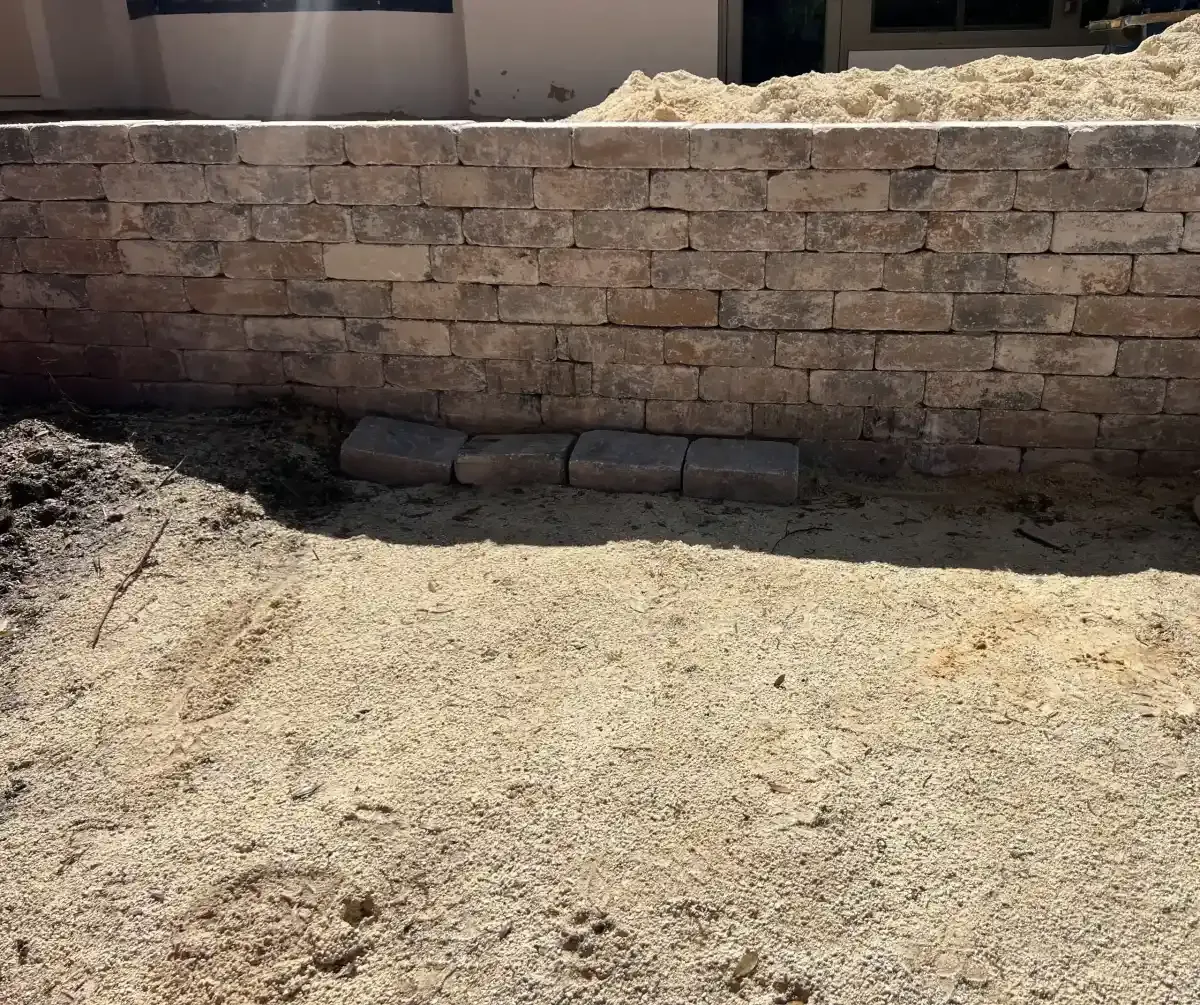 Stone retaining wall with a small alcove and dirt ground in a backyard or construction area.