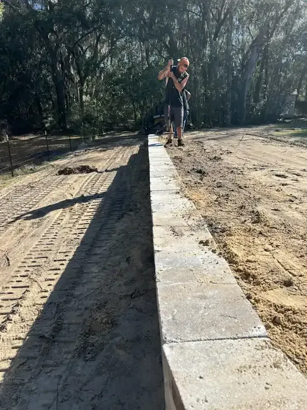 Person balancing on a narrow concrete beam in a sandy outdoor area with trees in the background