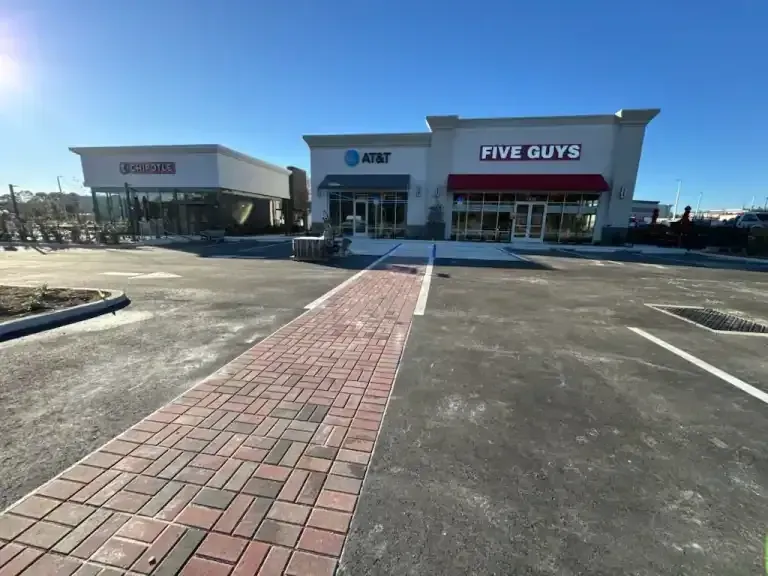 Shopping center with a Five Guys restaurant, brick walkway, and empty parking lot on a sunny day