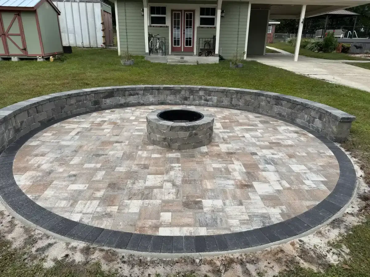 Circular stone fire pit with a low curved bench on a gravel patio in a backyard