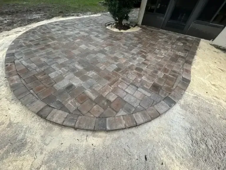 Curved brick paver patio beside a sandy yard and house entrance