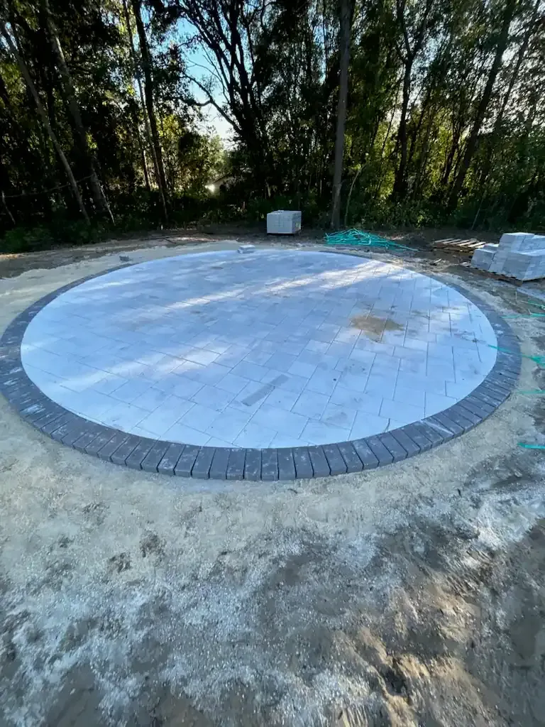 Circular white tiled pad in a wooded clearing, bordered by gray bricks and concrete.