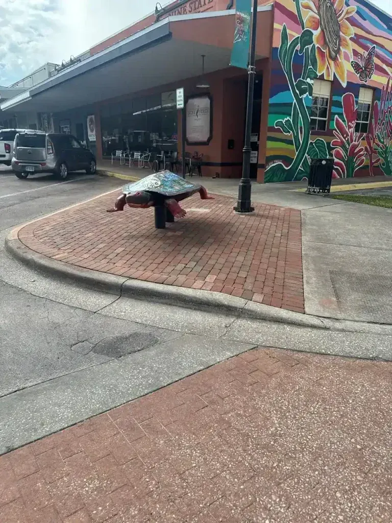 Turtle sculpture on a brick sidewalk beside a street mural and parked cars