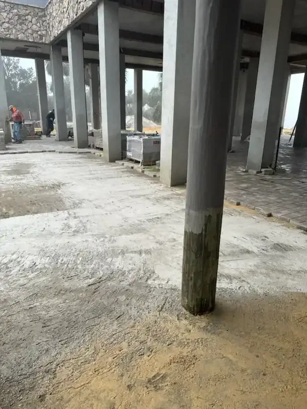 Concrete building under construction with pillars and a worker in the distance