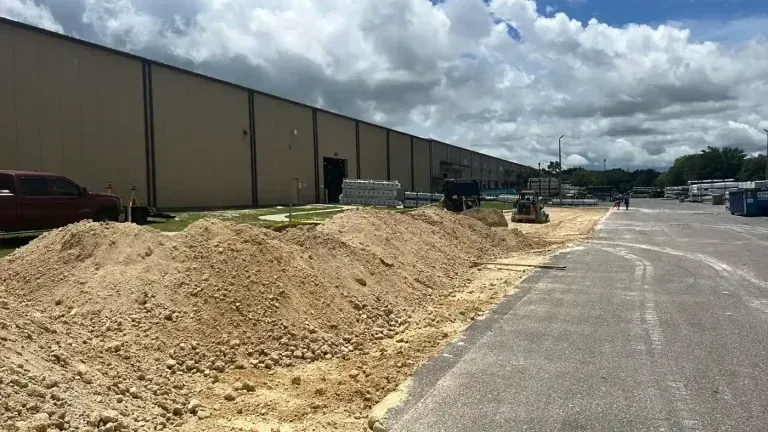 Large dirt pile beside an industrial building along a paved road under cloudy skies