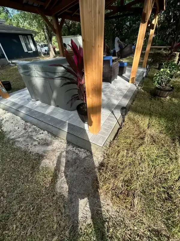 Covered patio with wooden posts, a car, and potted plants beside a grassy yard.