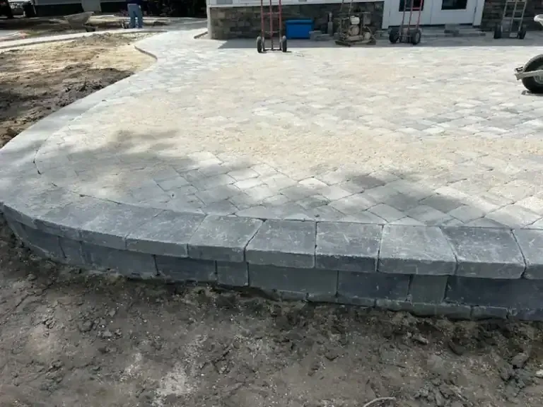 Curved gray stone patio edging a light concrete driveway near a house under construction