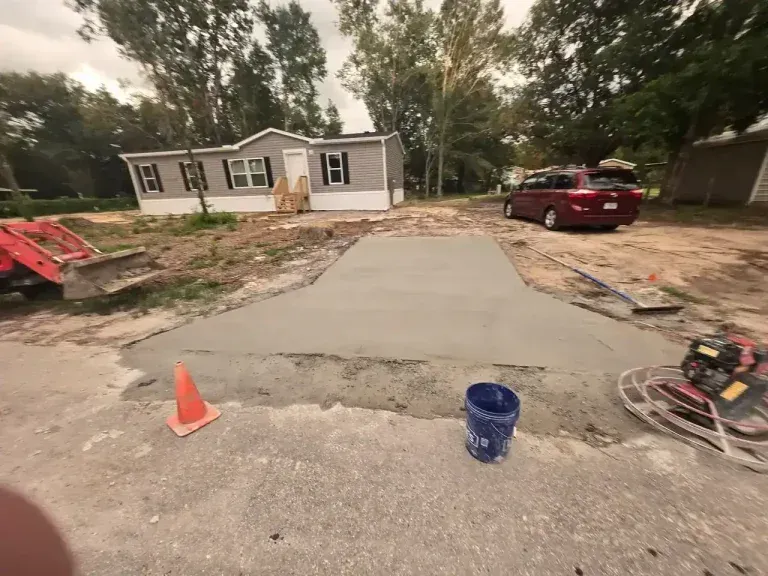 Driveway repair in progress outside a white house, with orange cones, tools, and a red SUV parked nearby.