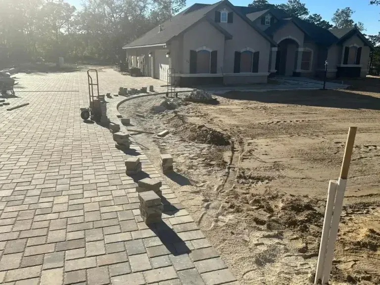 Residential construction site with paver walkway, dirt landscaping, and a partially finished house