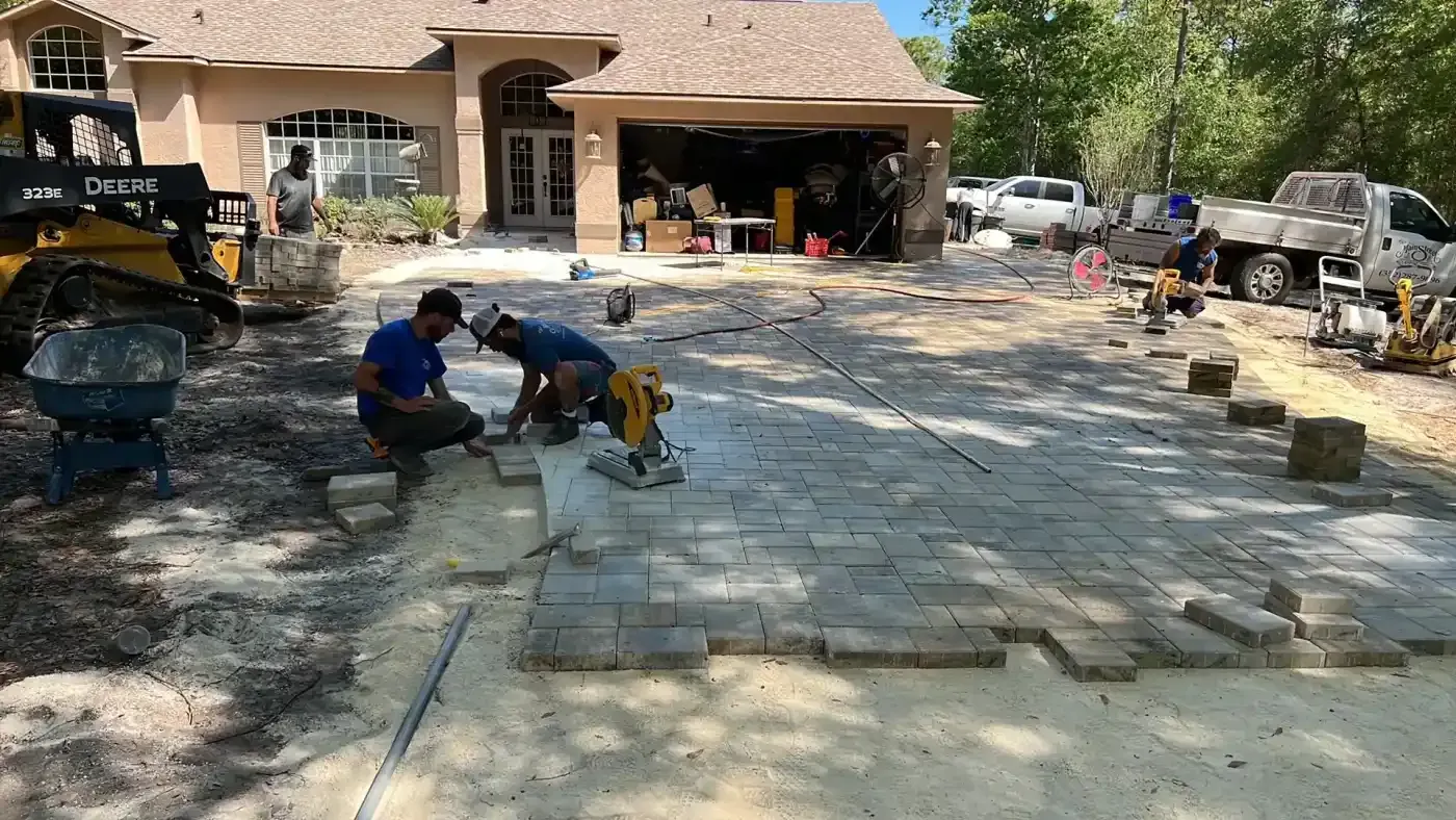 Workers laying gray pavers in a suburban driveway under construction